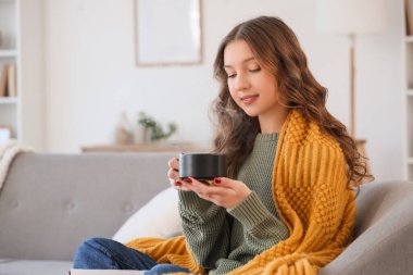 Evdeki koltukta oturan bir fincan lezzetli kahveyle güzel, genç ve mutlu bir kadın.