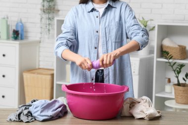 Genç bir kadın evdeki plastik havuzda ıslak giysilerini sıkıyor.