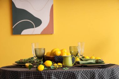 Yemek odasındaki sarı duvarın yanında bir sürü taze limonla süslenmiş şık bir masa.