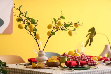 Yemek odasındaki sarı duvarın yanında taze narenciye ve güzel limon dallarıyla süslenmiş şık bir masa.