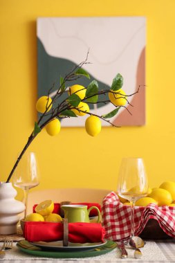Yemek odasındaki sarı duvarın yanında taze narenciye ve güzel limon dallarıyla süslenmiş şık bir masa.