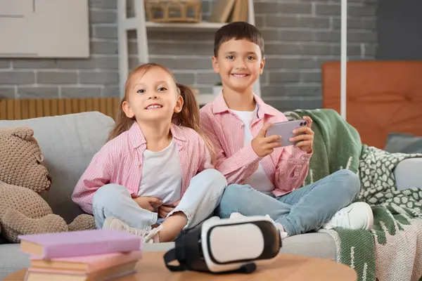 Cep telefonlu şirin çocuklar evdeki kanepede video oyunu oynuyorlar.