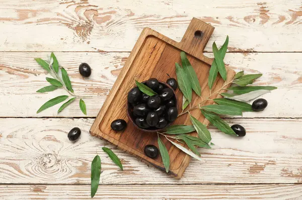 Lezzetli siyah zeytin tabağı ve hafif ahşap arka planda yapraklar.