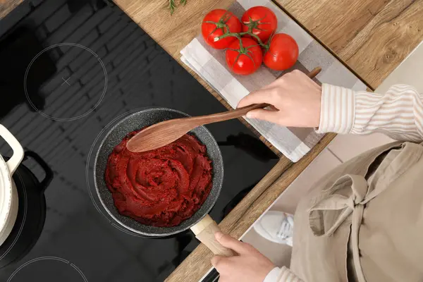 Kızartma tavasında domates ezmesi karıştıran genç bir kadın. Mutfakta kaşıkla.