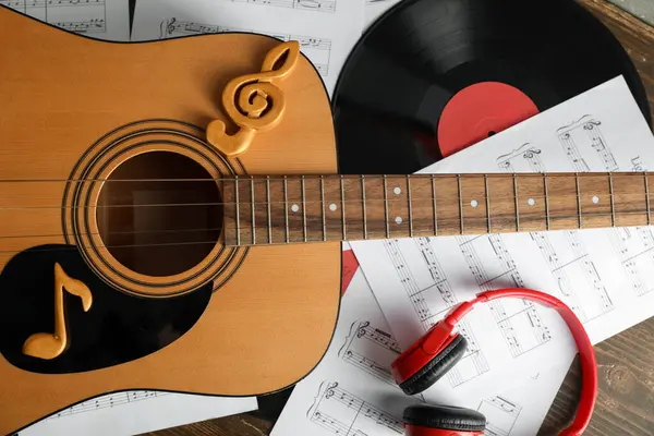 Gitar, müzik kağıtları, kulaklıklar ve plak diski ahşap masada, yakın plan.