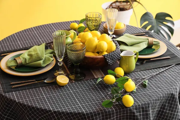 Yemek odasındaki sarı duvarın yanında bir sürü taze limonla süslenmiş şık bir masa.