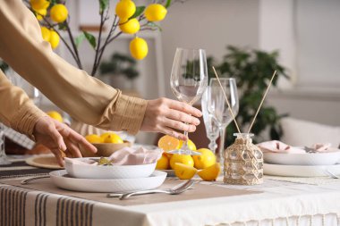 Masa dekorasyonu yapan genç bir kadın. Taze sitruslar, limon ağacı dalları ve yemek odasında bardaklar. Yakın plan.