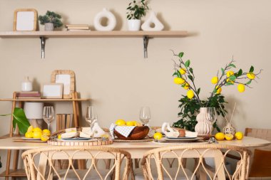 Yemek odasındaki bej duvarın yakınındaki güzel limon dalları ve taze limon ağaçlarıyla süslenmiş şık masa dekorasyonu.