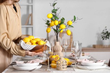 Yemek odasında bir kase taze limonla masa dekorasyonu yapan genç bir kadın.