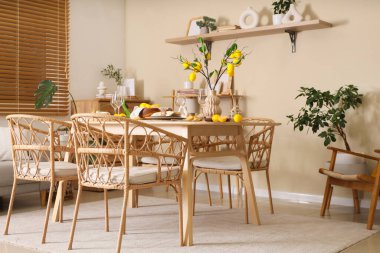 Yemek odasının içi masa düzeniyle, taze turunçgillerle ve bej duvarın yanında limon dallarıyla dolu.