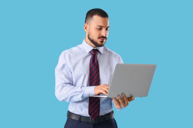 Kravatlı genç işadamı mavi arka planda dizüstü bilgisayar kullanıyor