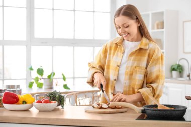 Mutfaktaki masada mantar kesen genç bir kadın.