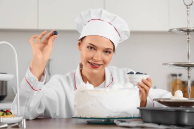 Kadın pastacı mutfakta yaban mersinli pasta yapıyor.