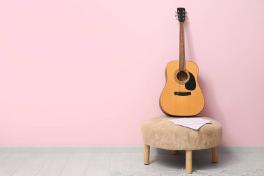 Renk duvarının yanındaki pouf 'ta akustik gitar ve müzik kağıtları
