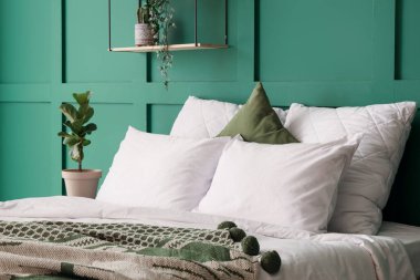 Yatak odasındaki yeşil duvarın yanında yumuşak yastıklı yatak