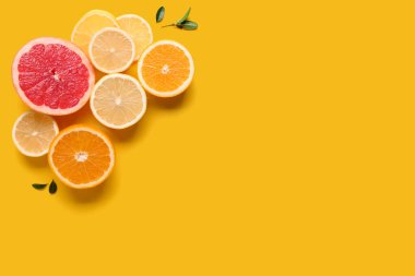 Farklı kesilmiş turunçgil meyveleri ve sarı arkaplanda yapraklar