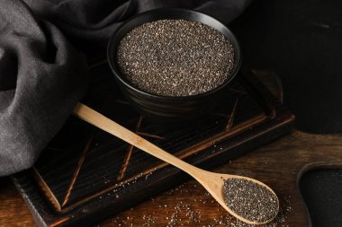 Siyah arka planda chia tohumları olan bir kase ve tahta kaşık.