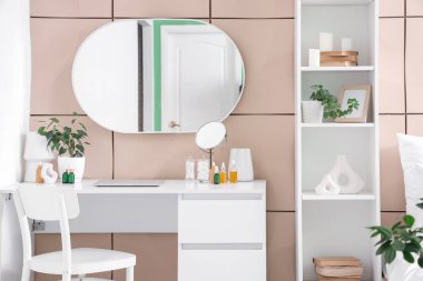 Yatak odasındaki bej fayans duvarının yanında makyaj masası ve kozmetik ürünler.