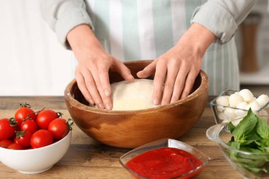 Mutfaktaki ahşap masanın yanında çiğ hamurlu ve pizza malzemeli bir kadın.