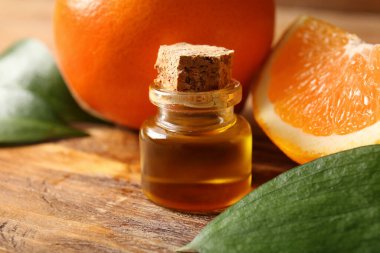 Yapraklı bir şişe portakal yağı ve ahşap arka planda taze meyveler, yakın plan.