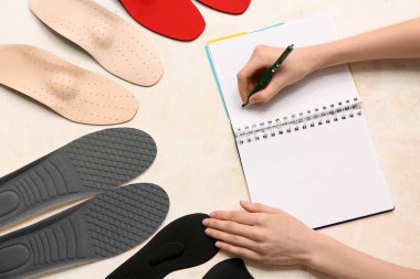 Ortopedik tabanlı bir kadın arka planda deftere yazı yazıyor.