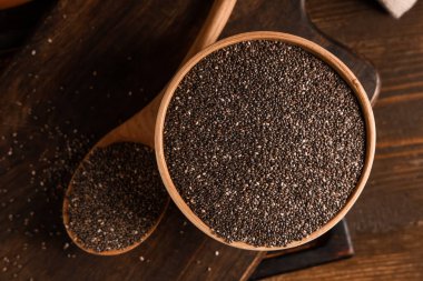 Ahşap zemin üzerinde chia tohumları olan kase ve kaşık.