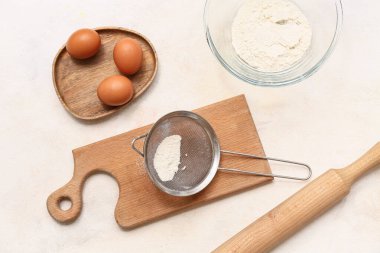 Un, ahşap tahta, merdane ve arka planda tavuk yumurtası olan metal elek.