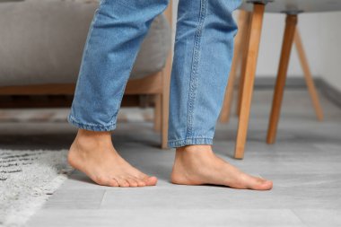 Çıplak ayaklı, kot pantolonlu, evde ısıtmalı kadın bacakları.