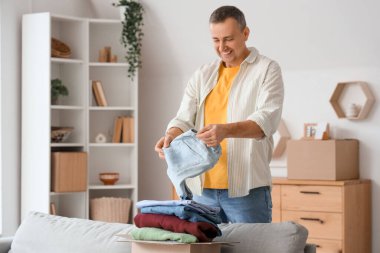 Olgun bir adam evinde giysileriyle birlikte kutuları açıyor.