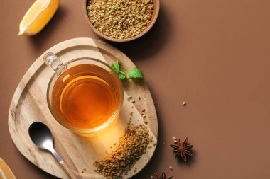 Limonlu bir bardak sıcak karabuğday çayı, kahverengi arka planda yıldız anason ve nane yaprakları.
