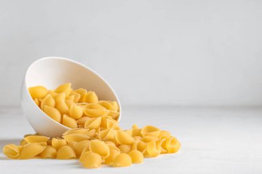 Beyaz arka planda çiğ makarna kabukları ile ters çevrilmiş kase.