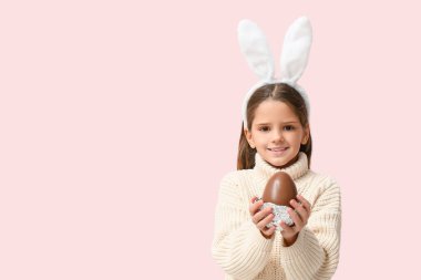 Pembe arka planda çikolata yumurtası olan tavşan kulaklı tatlı küçük kız.
