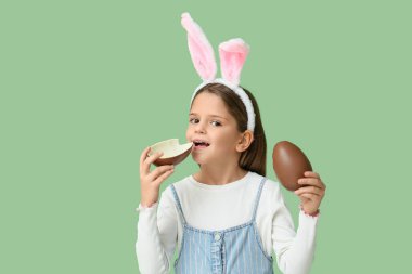 Yeşil arka planda yarım parça çikolata yumurtası olan tavşan kulaklı şirin küçük kız.