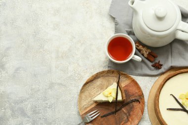 Tahta tabakta vanilya çiçekli tatlı cheesecake dilimi ve gri arka planda bir fincan çay