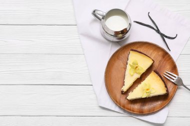 Beyaz ahşap zemin üzerinde tatlı vanilyalı cheesecake ve sütle dolu bir tabak.