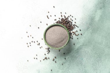 Arkaplanda karabiber tozu ve karabiber olan bir kase.