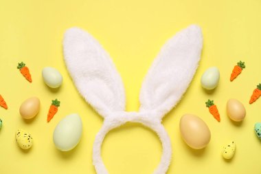 Paskalya yumurtalı tavşan kulakları ve sarı arka planda dekoratif havuçlar.
