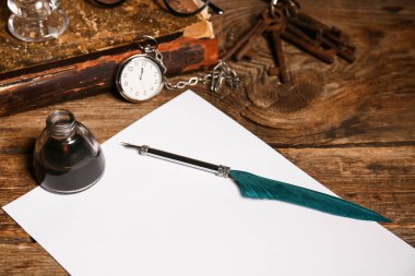 Kağıt çarşaf, tükenmez kalem, mürekkep hokkası, anahtarlar ve ahşap arka planda cep saati olan eski bir kitap.
