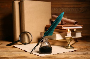 Ağaç zemin üzerinde kalem, mürekkep hokkası, büyüteç ve parşömen bulunan kitaplar