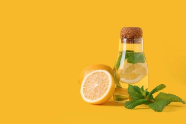 Sarı zemin üzerinde limon ve nane yaprakları olan bir kavanoz su.