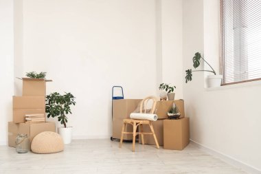 Taşınma gününde içinde büyük yatak, ev bitkileri ve hasır sandalye olan karton kutular.