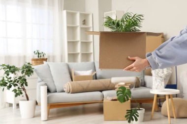 Taşındığı gün oturma odasında çiçekli karton kutu taşıyan kadın, yakın plan.