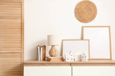 Evin şeklindeki mum tutucuları, kitaplar ve lambalar oturma odasının iç tarafındaki beyaz duvarın yanındaki çekmecelerin üzerinde.