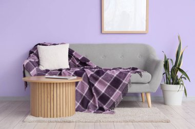 Mor duvarın yanındaki kanepede çiçekli kahve masası ve şık ekose.