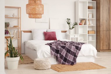 Yatağında raf üniteleri, ev bitkileri ve mor battaniye olan modern yatak odası.