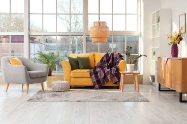 Pencereye yakın sarı kanepe üzerinde koltuk, klozet ve mor ekoseli modern oturma odası.