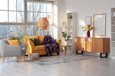 Modern oturma odasının içinde, koltuğu, raf üniteleri ve sarı koltukta mor ekoseli.