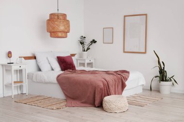 Modern yatak odasının içinde bitkiler, komodinlerin yanında yatağın üzerinde mor bir battaniye.