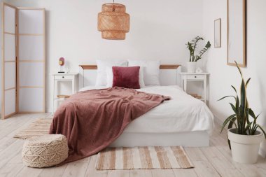 Modern yatak odasının içinde bitkiler, komodinlerin yanında yatağın üzerinde mor bir battaniye.