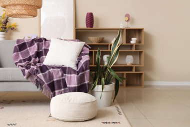 Modern oturma odasının içinde raf ünitesi, ev bitkileri ve gri koltukta mor ekose.